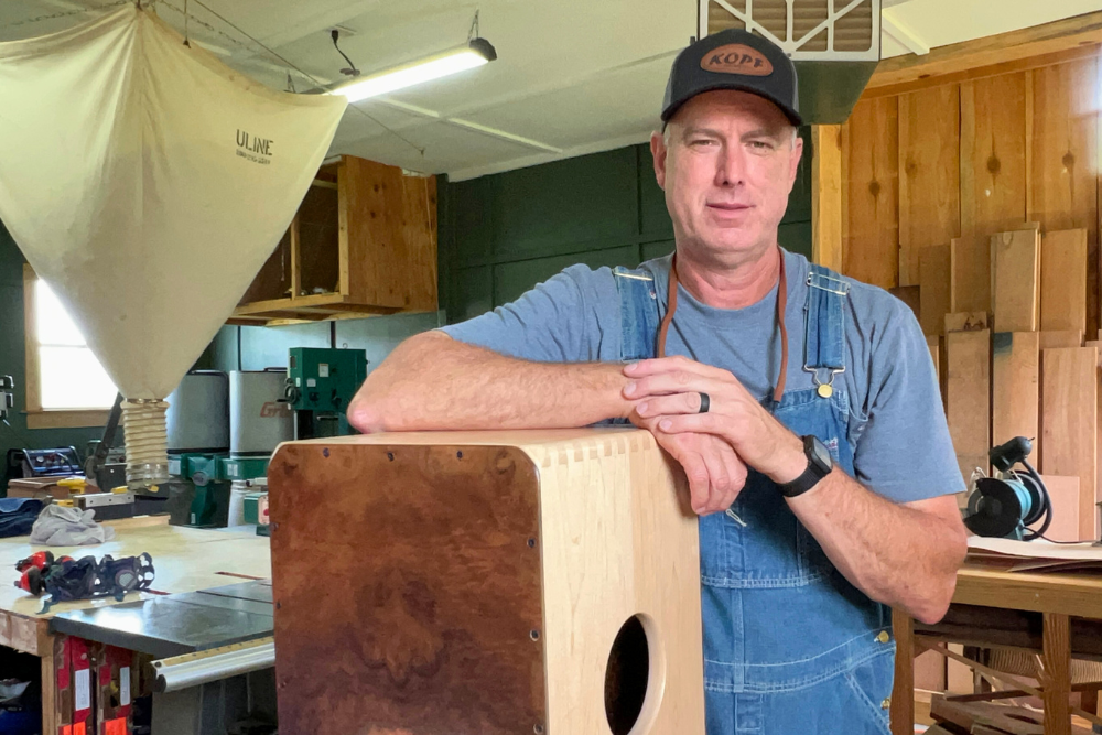 Stephen Head standing in his percussion workshop with a finished cajón, reflecting his handcrafted approach to drum making.
