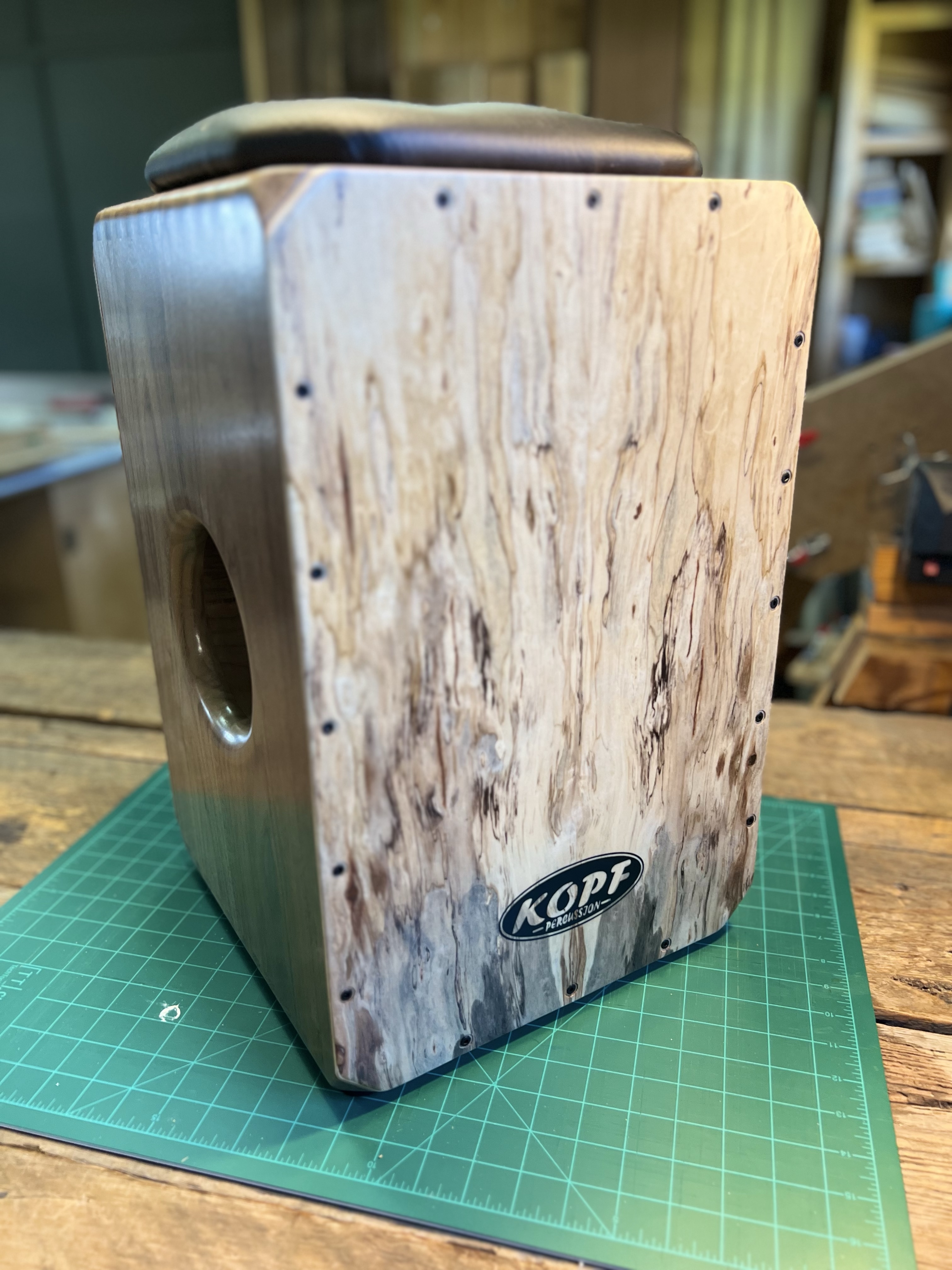 Full view of the finished handcrafted cajon with a walnut body, spalted maple faceplates, integrated bass port, and upholstered seat.