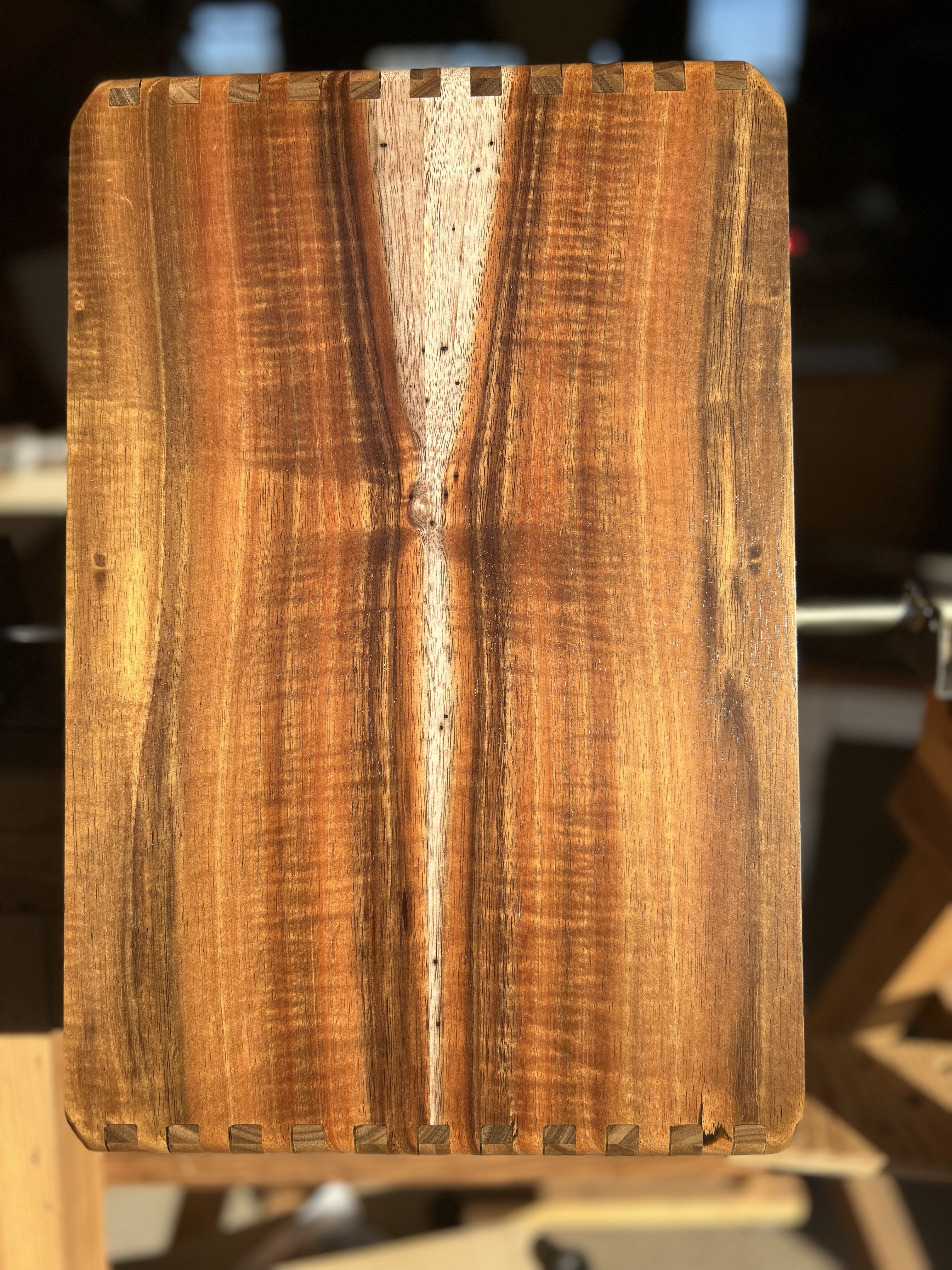 Koa cajon side panel with visible curl and joinery A koa side panel for a handcrafted cajon, showing the natural curl in the grain and the precision of the joinery under direct shop light.