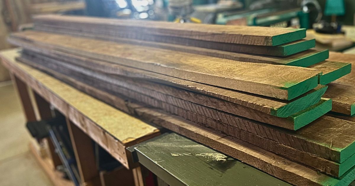 Stack of rough walnut lumber on a workbench, the starting point for handcrafted walnut Cajons by Kopf Percussion.